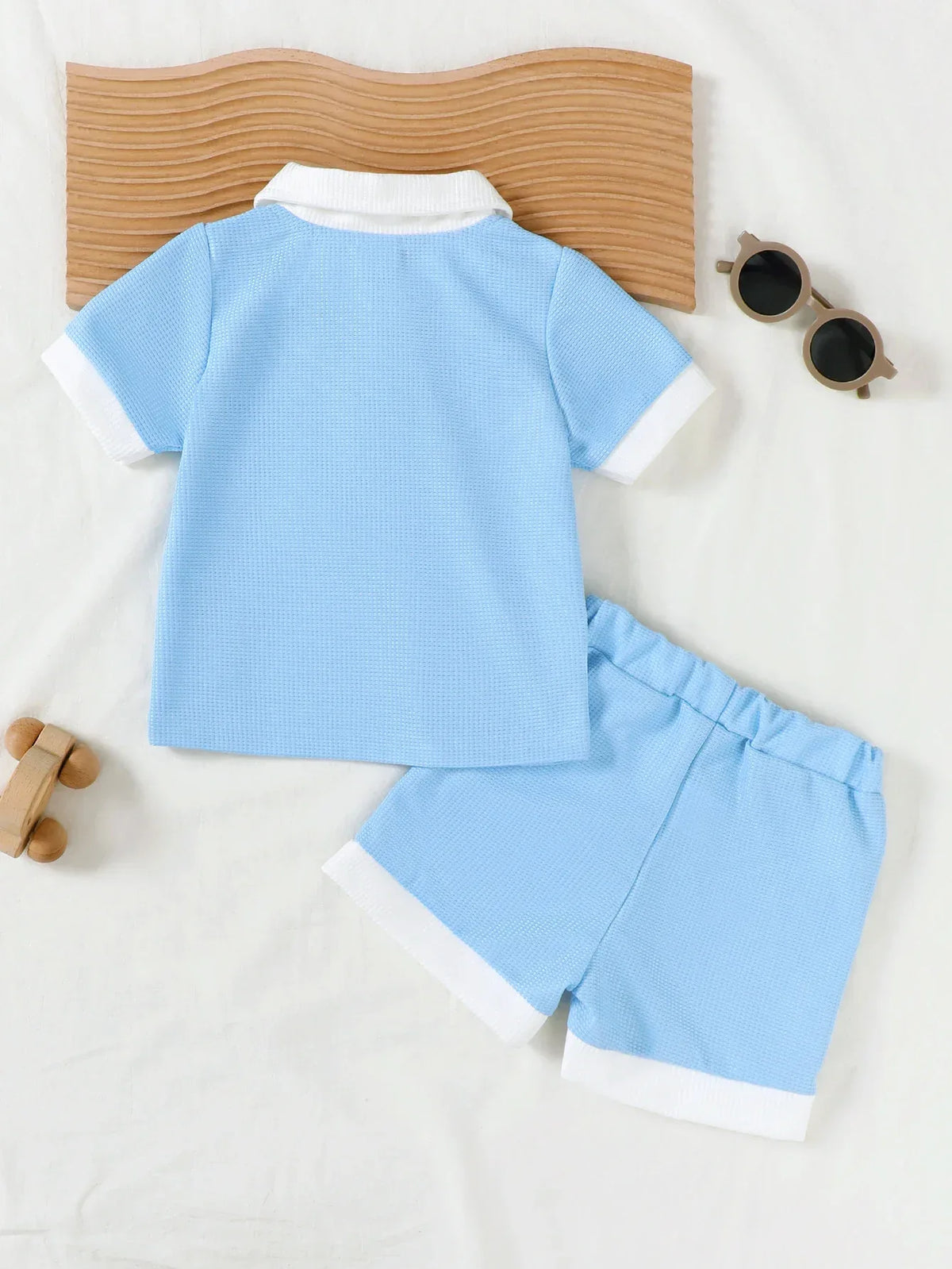 light blue toddler knit shorts set with white collar and cuffs laid flat with sunglasses and wooden toy