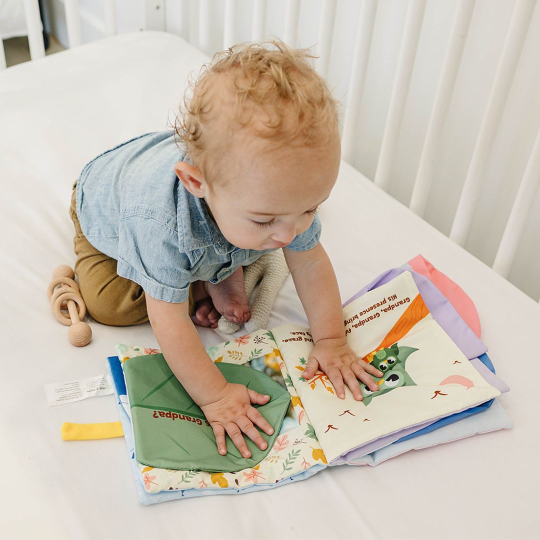 baby boy in blue shirt and brown pants playing with colorful interactive Peek-A-Photo book