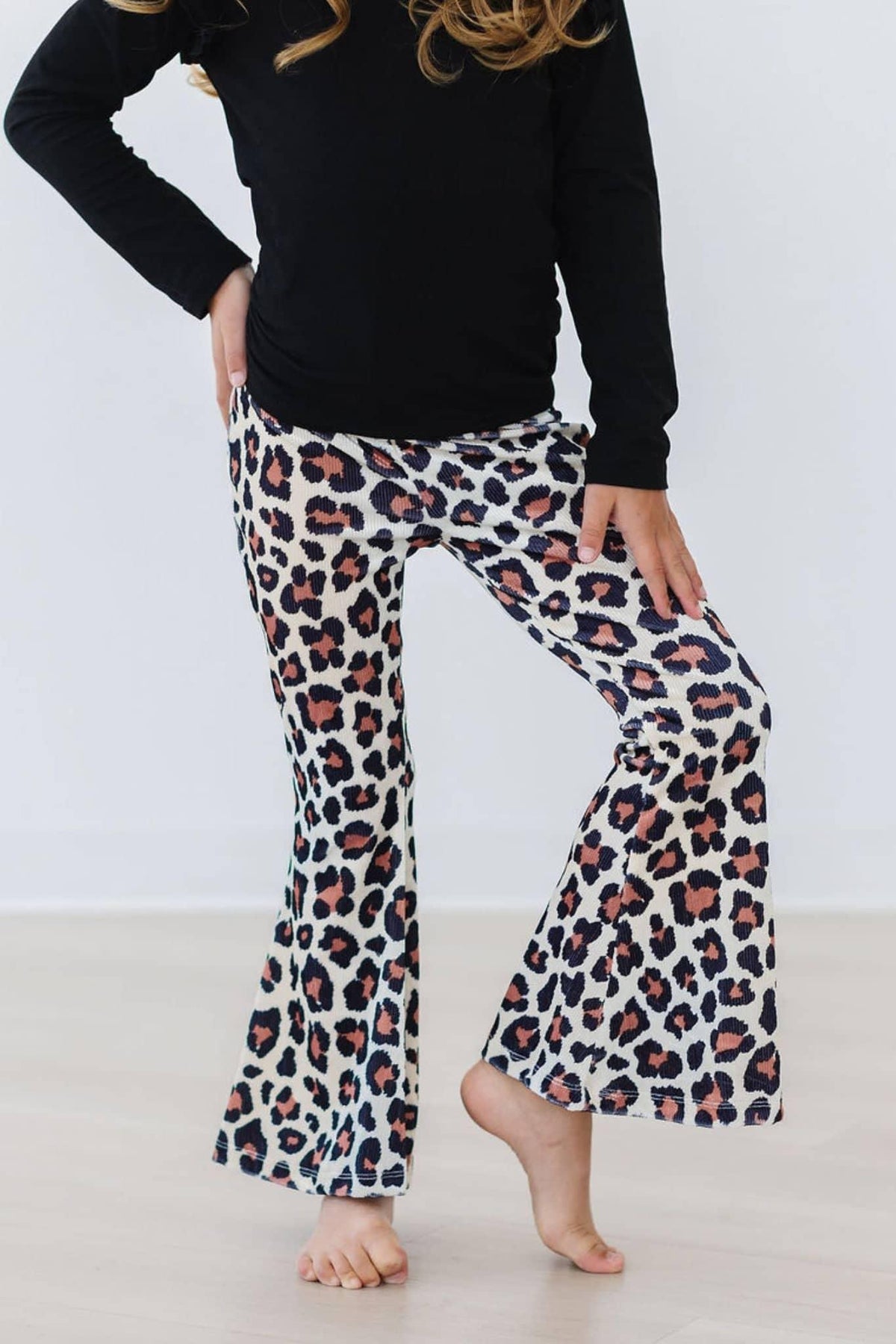 toddler wearing leopard print toddler velvet bell bottom pants standing barefoot with one leg raised