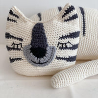 Close up of a white crochet tiger with dark stripes and closed eyes, resting in a relaxed pose.