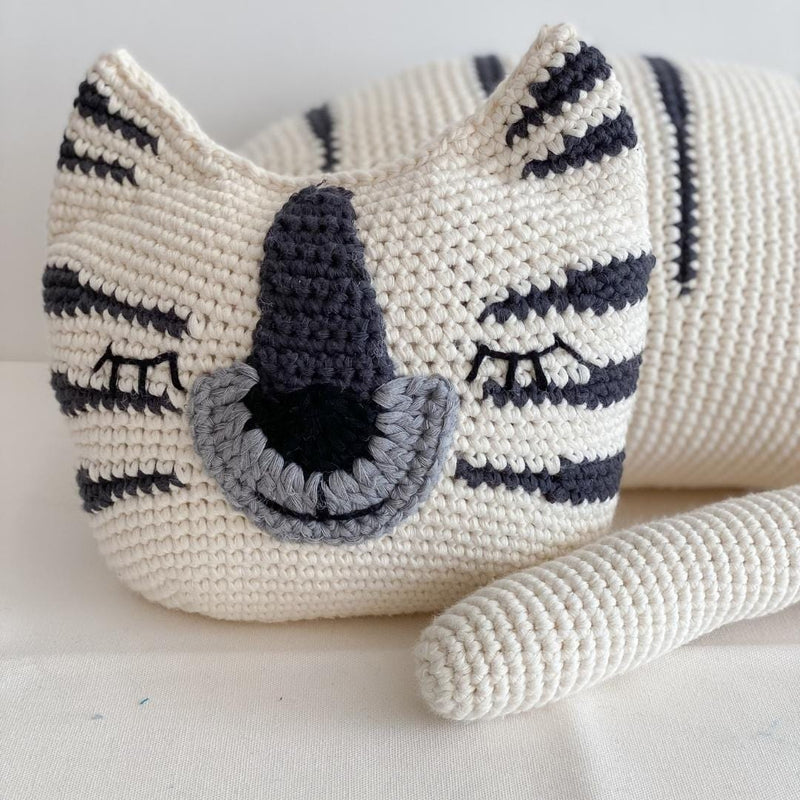 Close up of a white crochet tiger with dark stripes and closed eyes, resting in a relaxed pose.