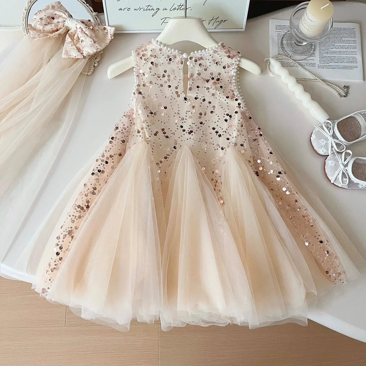 Beige sequin sleeveless tulle party dress for girls displayed on a hanger with matching headband and shoes