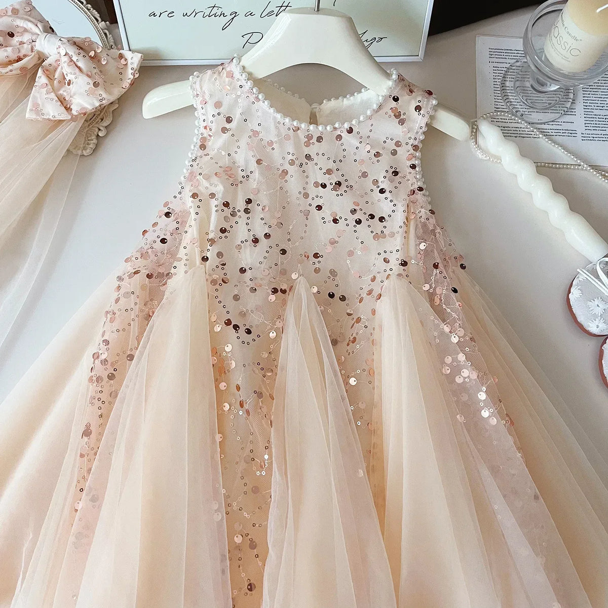 pink sequin tulle party dress for girls hanging on white hanger with matching bow headband