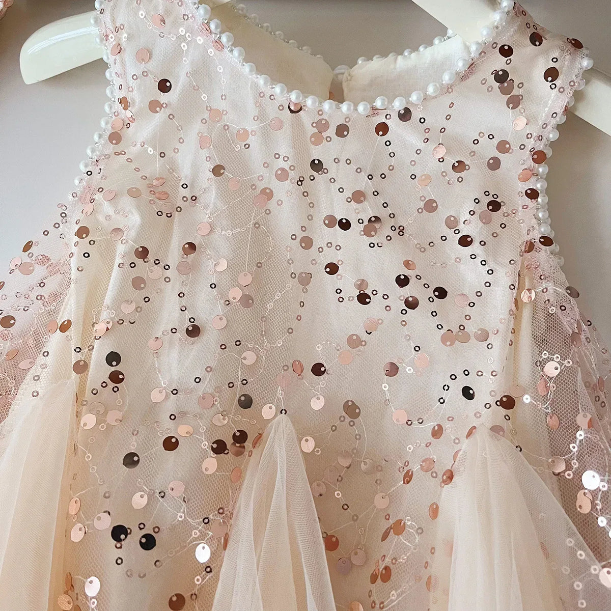 close-up of a cream tulle party dress for girls with pink and brown sequins and pearl trim on hanger