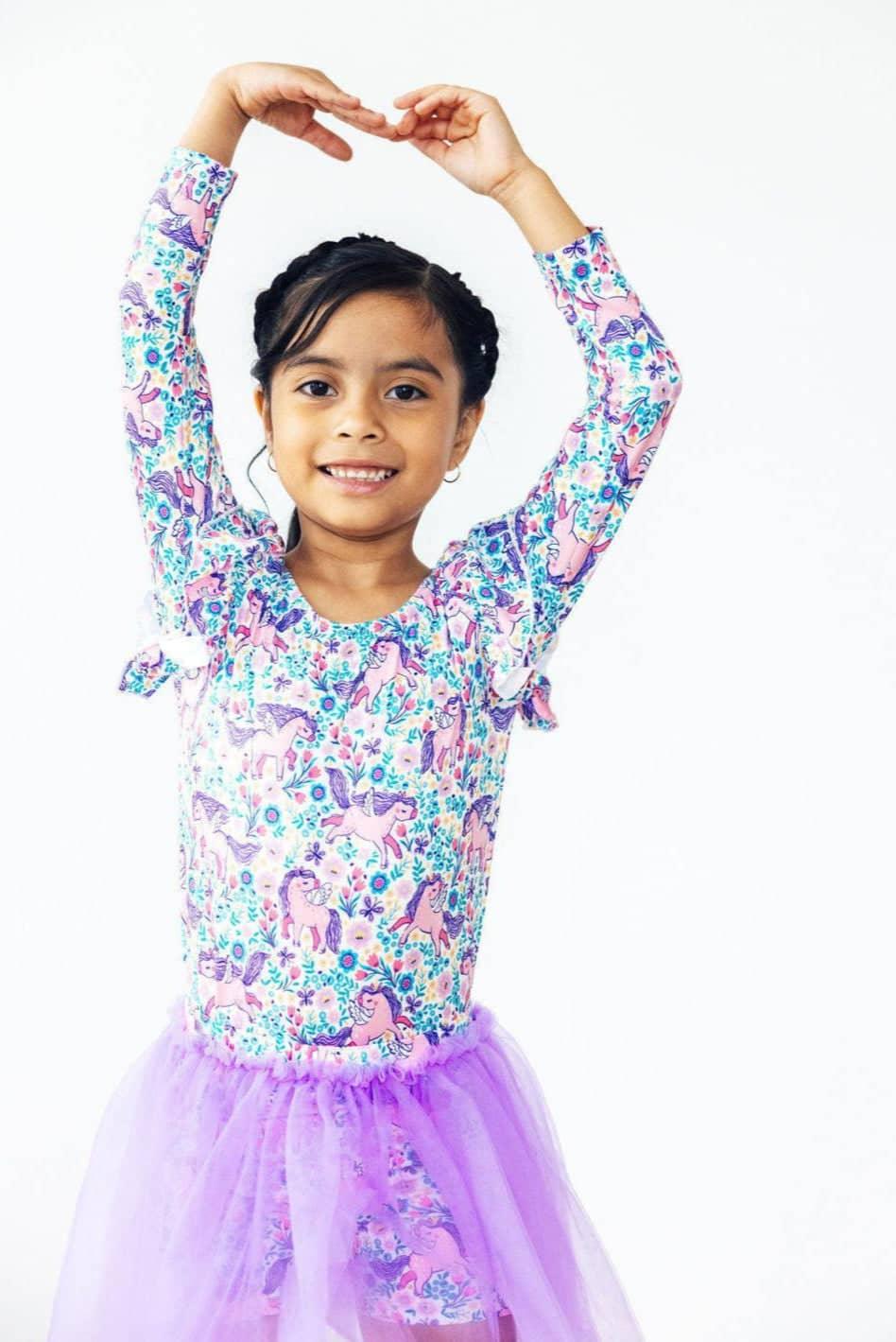 girl wearing purple tutu shorts for girls and long sleeve unicorn print top posing with arms raised