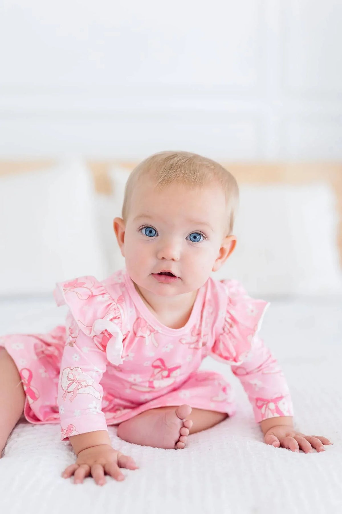 baby girl wearing pink twirl bodysuit with 3/4 flutter sleeves sitting on white bed