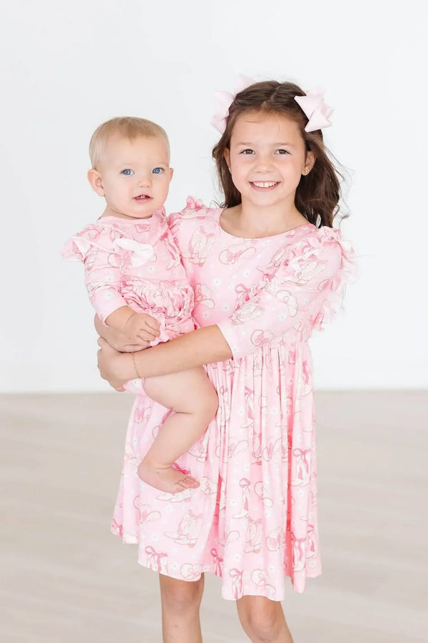 toddler wearing pink twirl bodysuit with 3/4 flutter sleeves held by smiling older girl