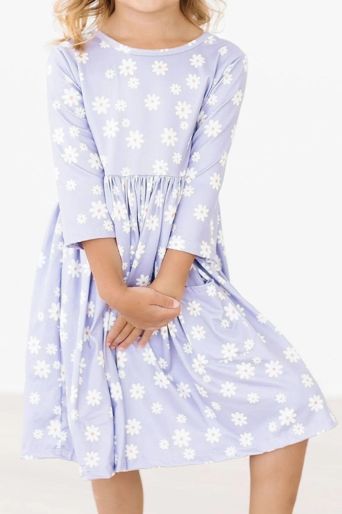 girl wearing lavender Mila & Rose twirl dress for girls with white daisy print holding dress