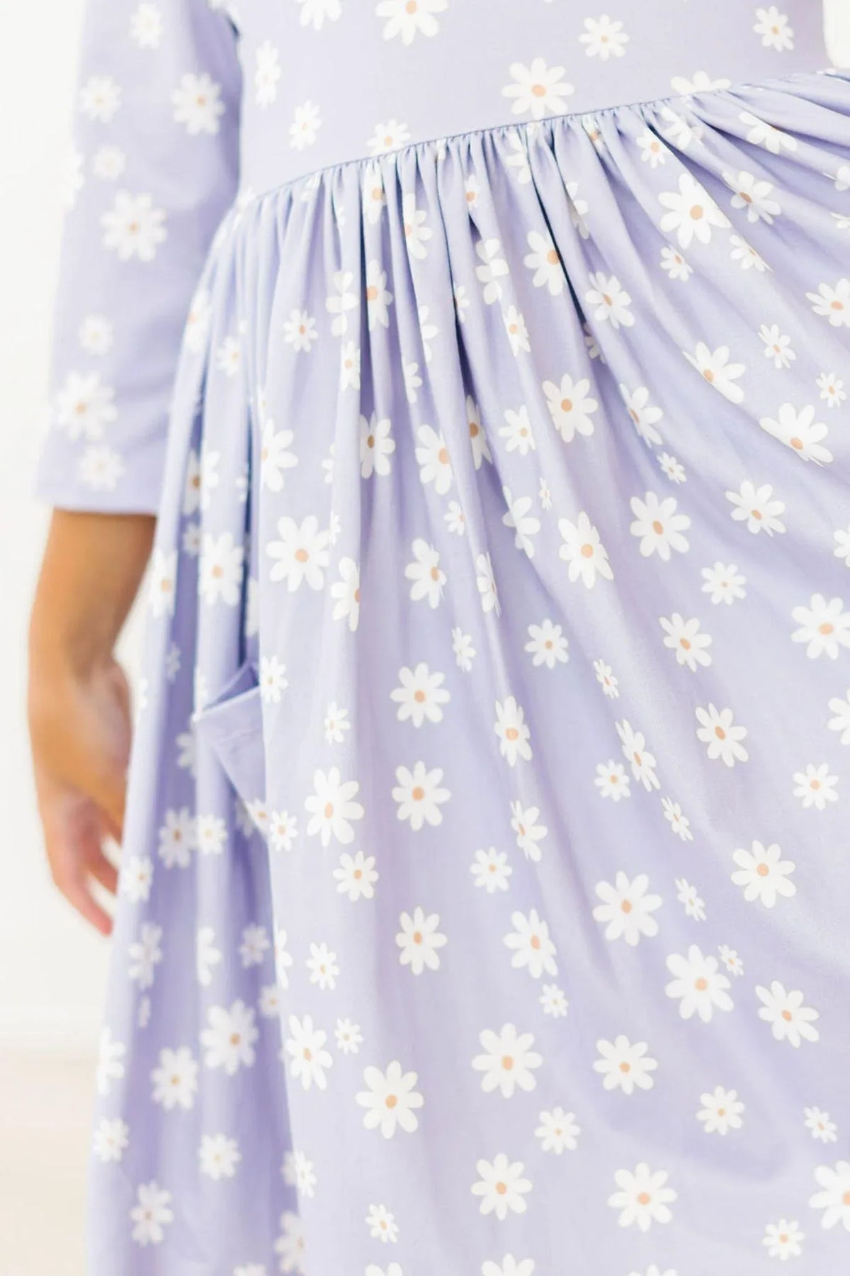 Girl wearing lavender Mila Rose twirl dress for girls with white daisy print holding pocket