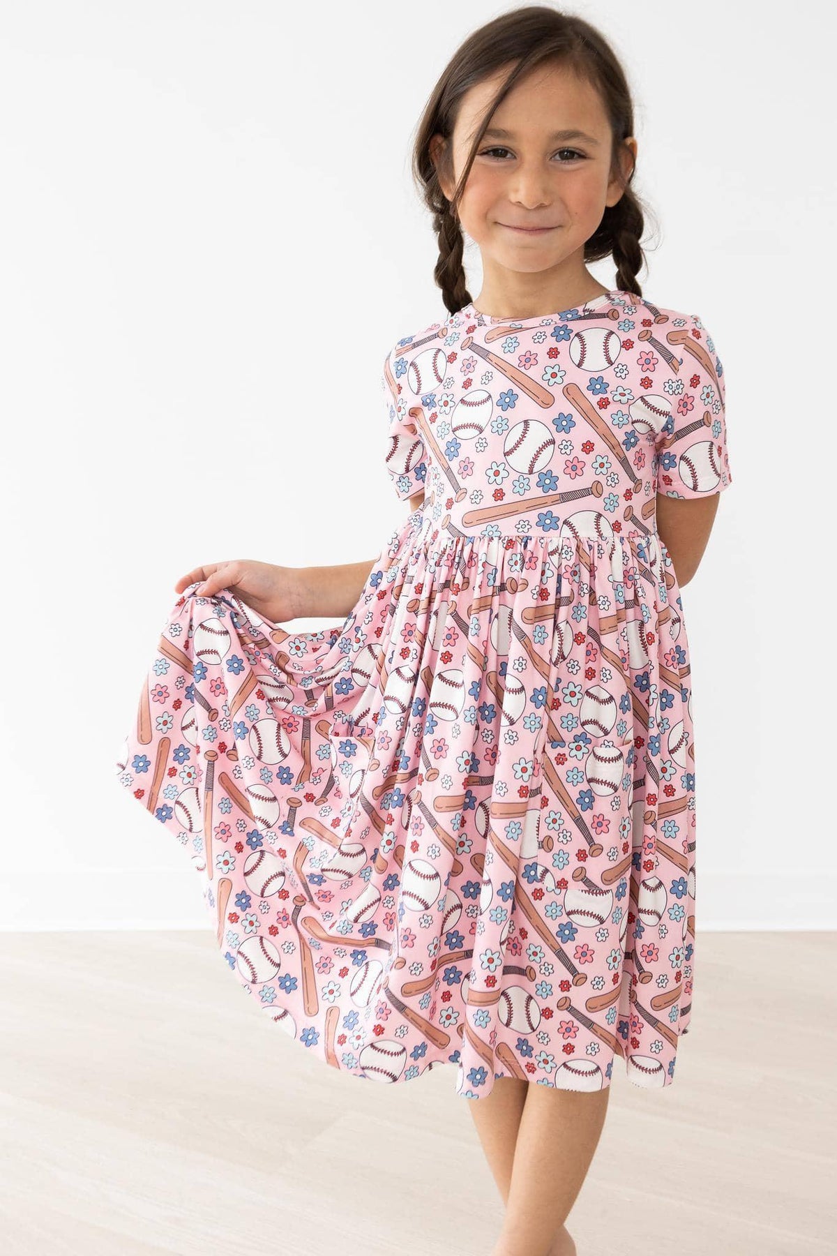 young girl wearing pink patterned twirl dress for girls holding skirt while smiling