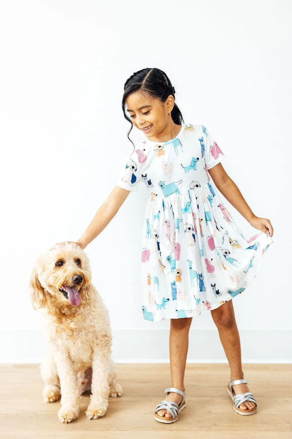 young girl wearing white twirl dress for girls with colorful animal prints holding skirt and petting dog
