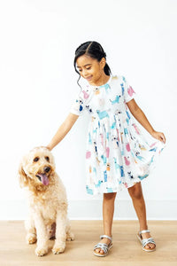 young girl wearing white twirl dress for girls with colorful animal prints holding skirt and petting dog