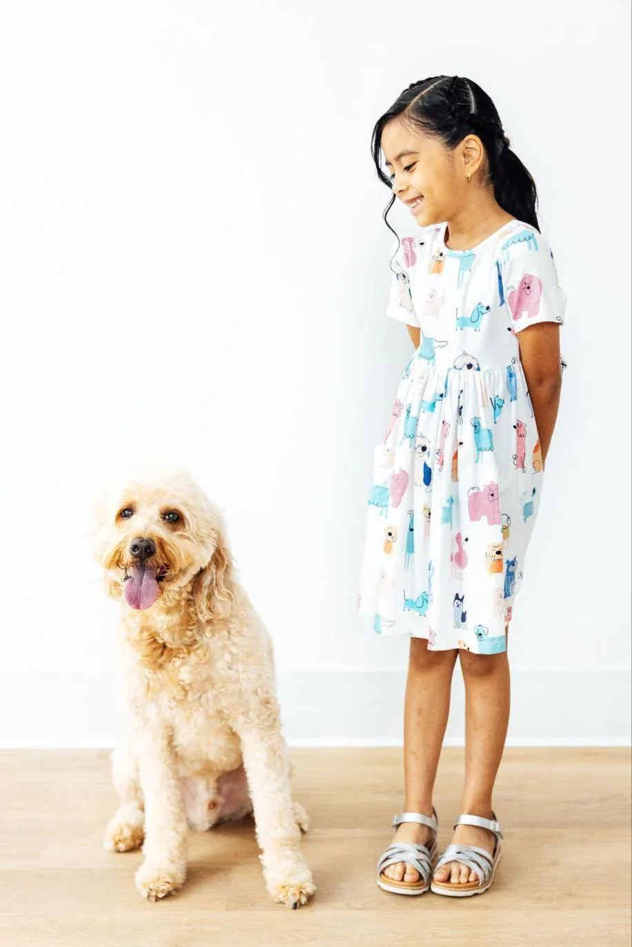 young girl wearing white twirl dress for girls with colorful animal prints standing next to a tan dog