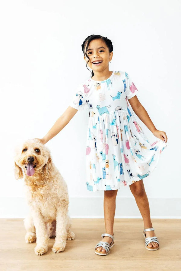 Girl wearing white Mila & Rose twirl dress for girls with colorful animal prints holding the hem and standing next to a dog