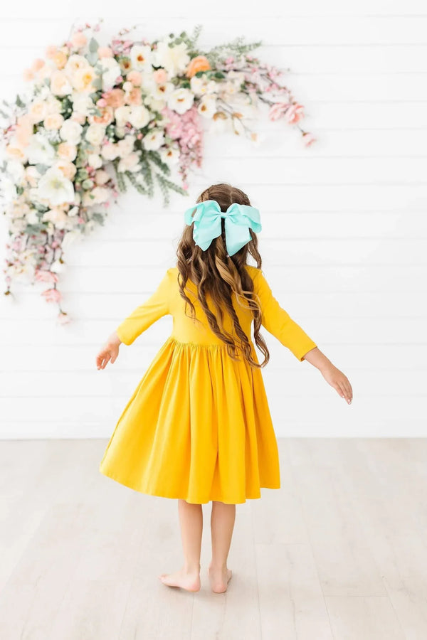 Young girl wearing yellow twirl dress for girls with 3/4 sleeves and blue hair bow spinning indoors
