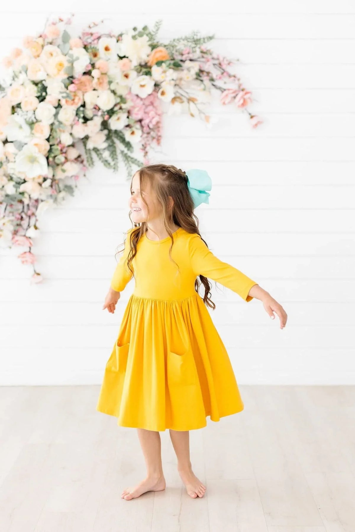 young girl wearing yellow twirl dress for girls spinning barefoot indoors with blue bow in hair