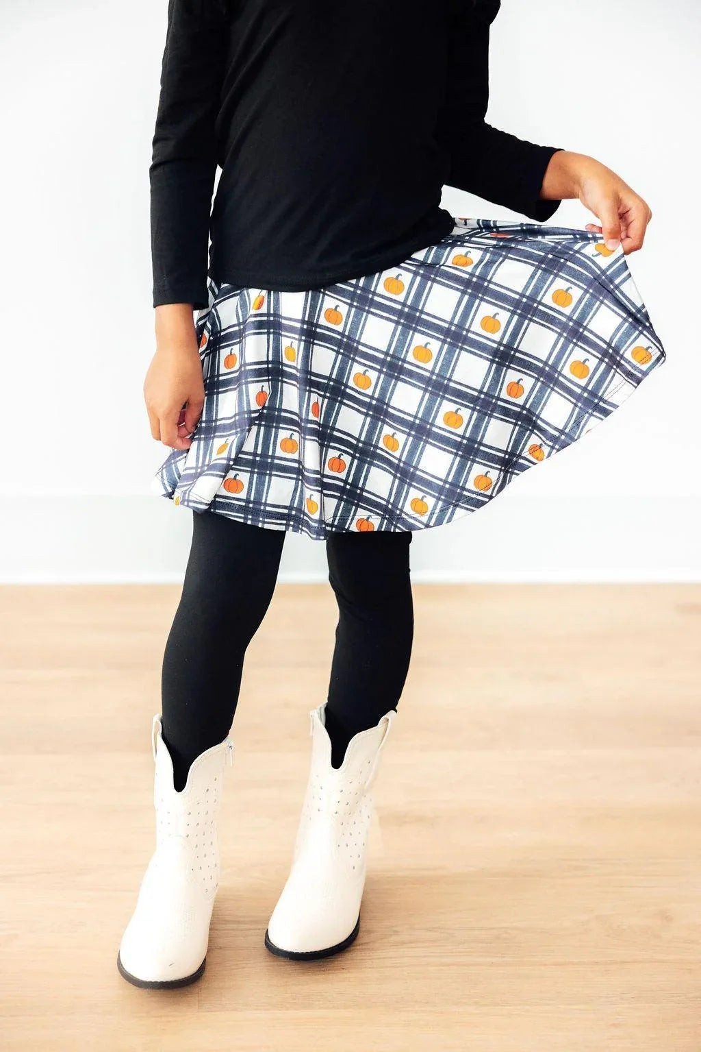 Girls black twirl skegging with white and blue plaid skirt featuring small orange pumpkin pattern