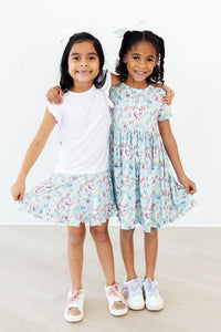 Two young girls smiling with arms around each other wearing unicorn dress for toddlers in pastel colors, twirling and posing
