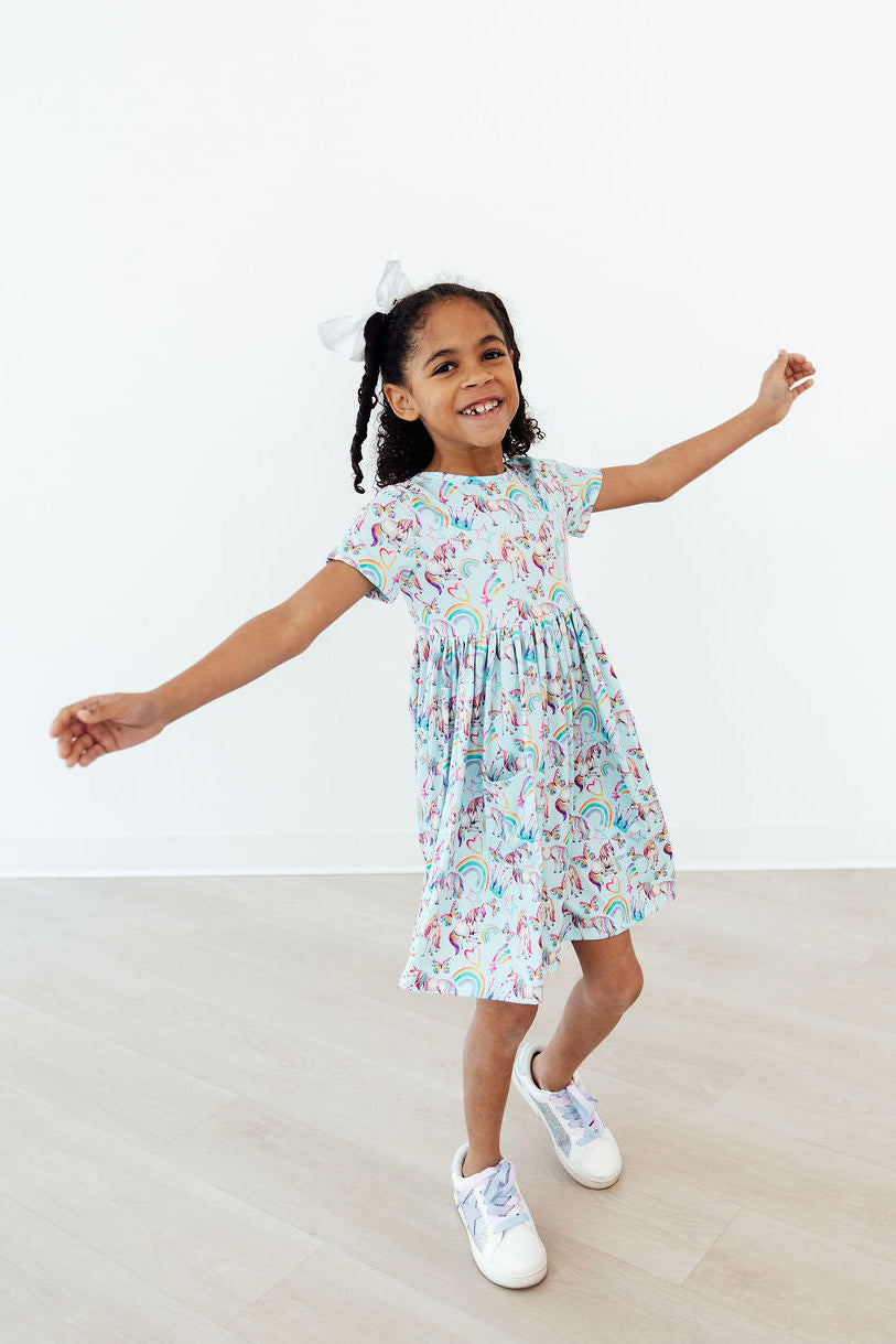 smiling toddler girl twirling in a white unicorn dress for toddlers with colorful rainbows and unicorns