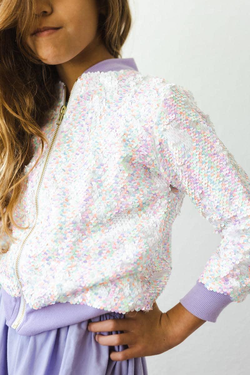 girl wearing white and pastel unicorn sequin jacket for girls with lavender cuffs and collar posing with hand on hip