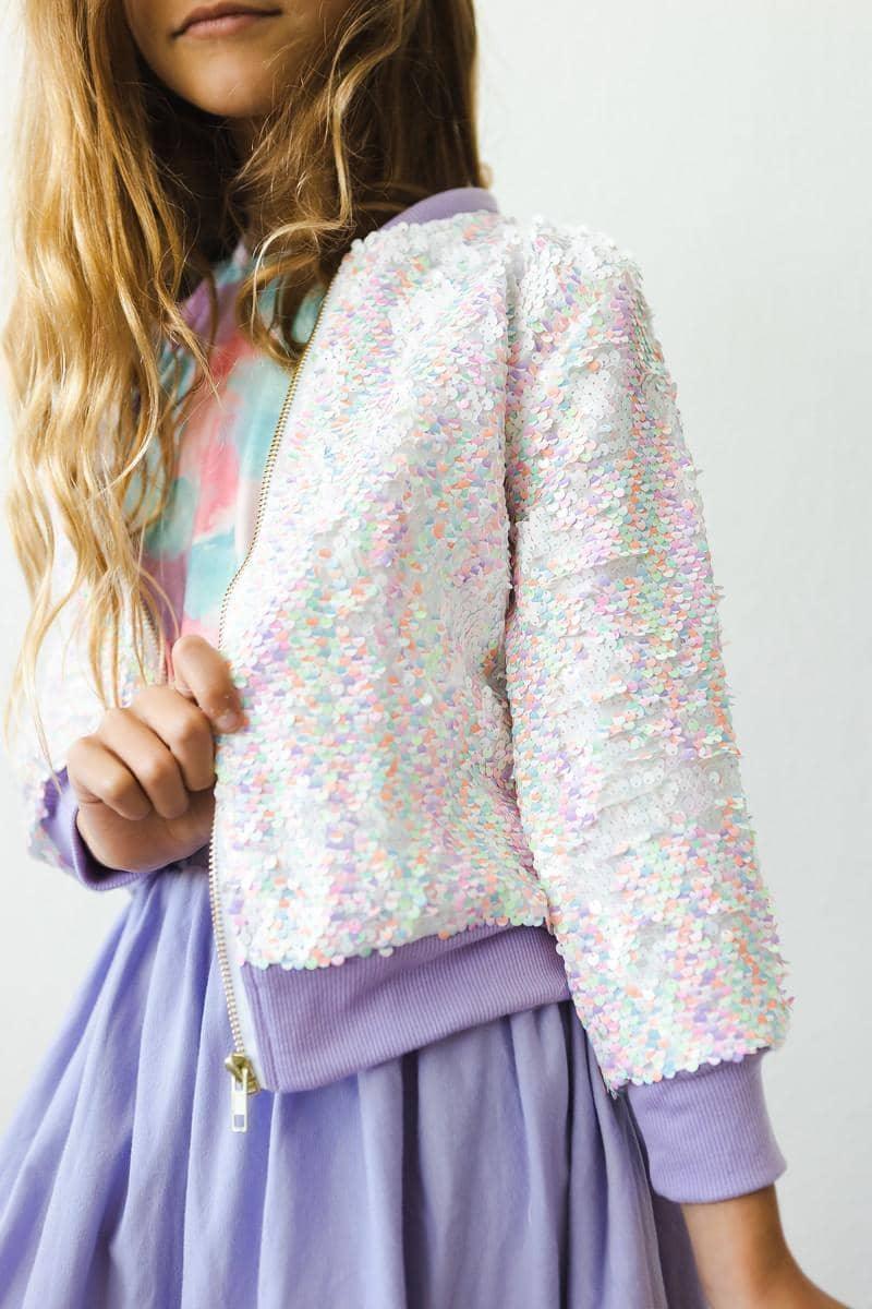 girl wearing Mila & Rose unicorn sequin jacket for girls in white and pastel colors standing with hand on jacket zipper