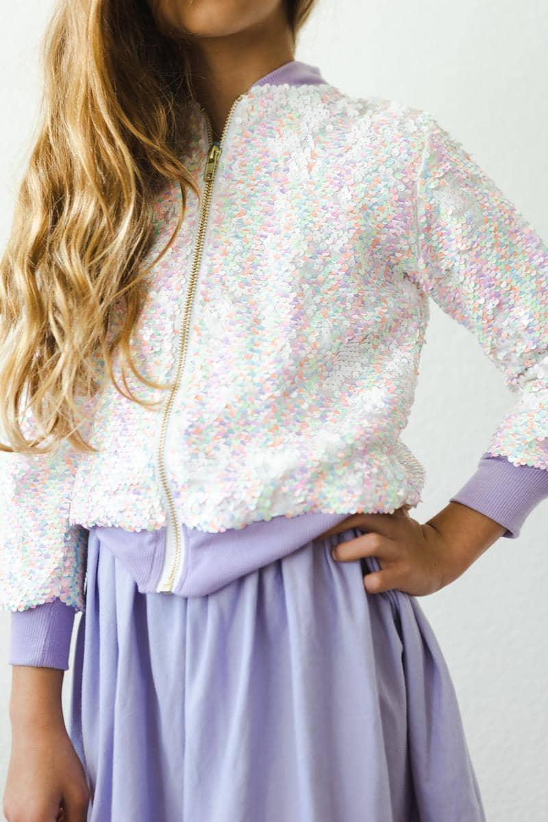 Girl wearing white and pastel unicorn sequin jacket for girls with lavender cuffs and skirt posing with hand on hip