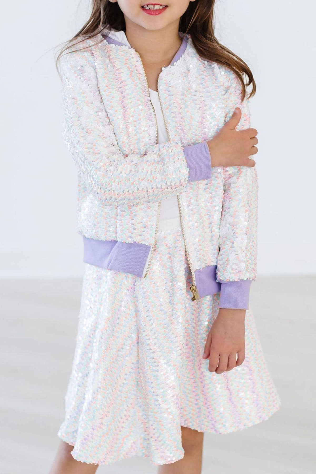 girl wearing white unicorn sequin jacket for girls with lavender cuffs and collar standing with arms crossed