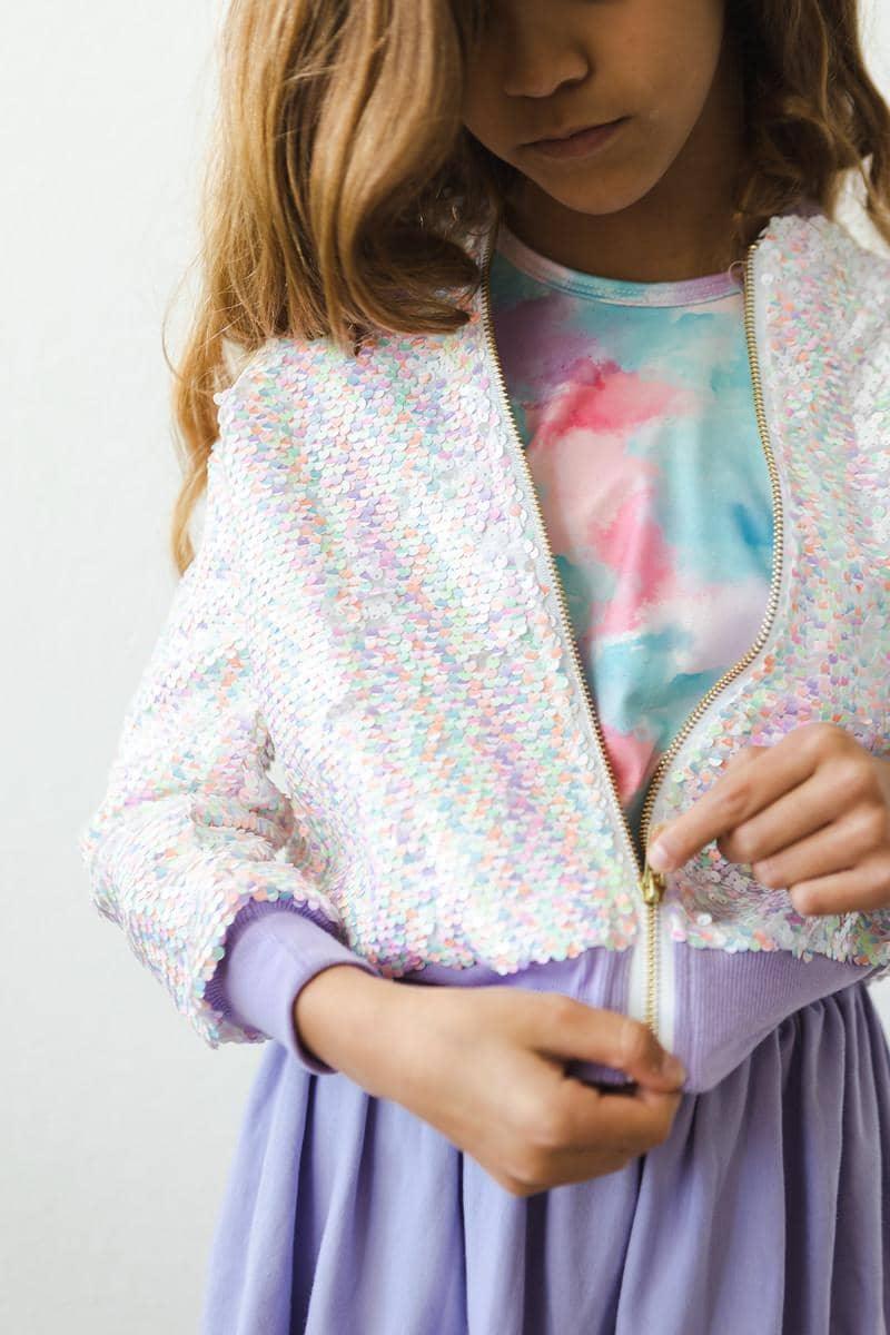 girl wearing unicorn sequin jacket for girls in pastel colors zipping up over tie-dye shirt