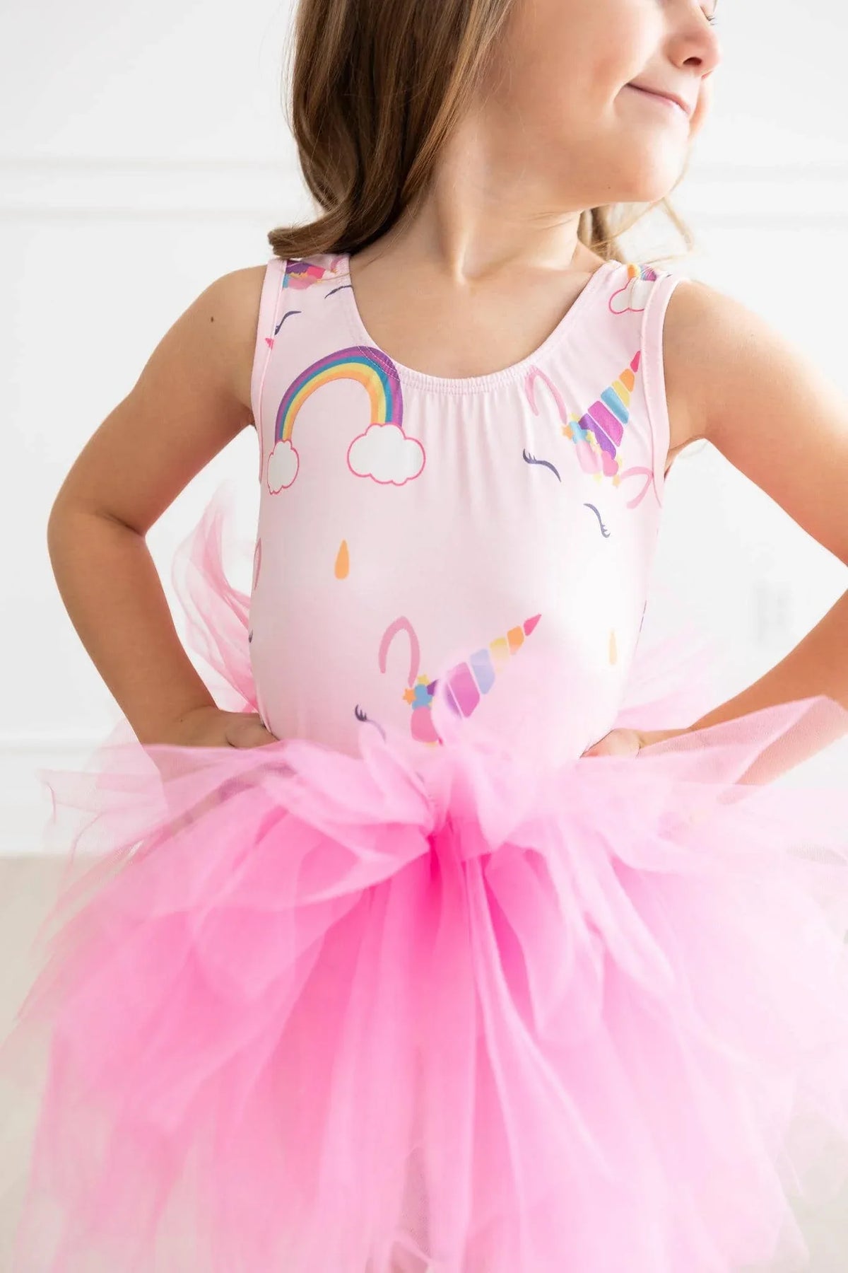 young girl wearing pink unicorn tutu leotard for girls with rainbow and unicorn prints posing with hands on hips