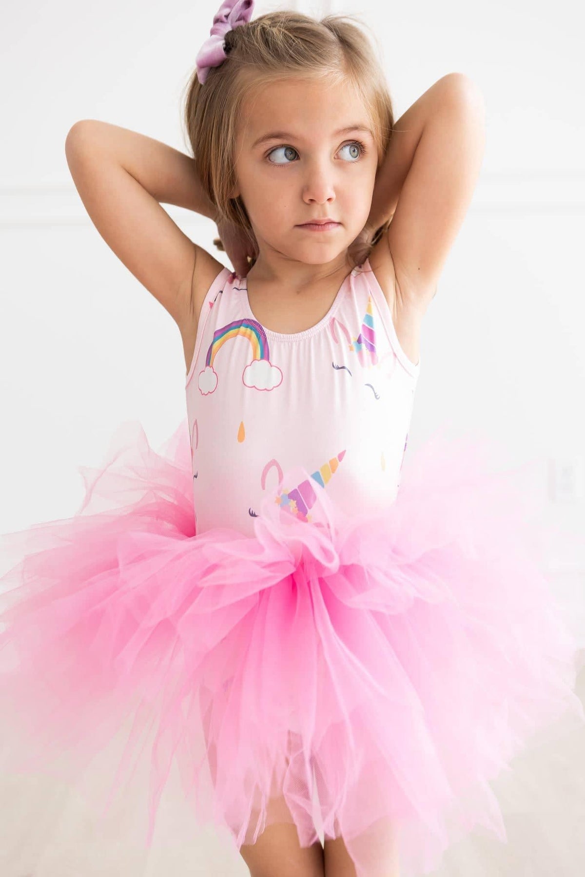 young girl wearing pink unicorn tutu leotard for girls with rainbow design posing with arms behind head