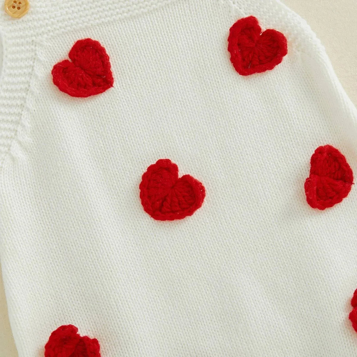 White cotton Valentine's Day baby romper with red knitted heart patterns and wooden button