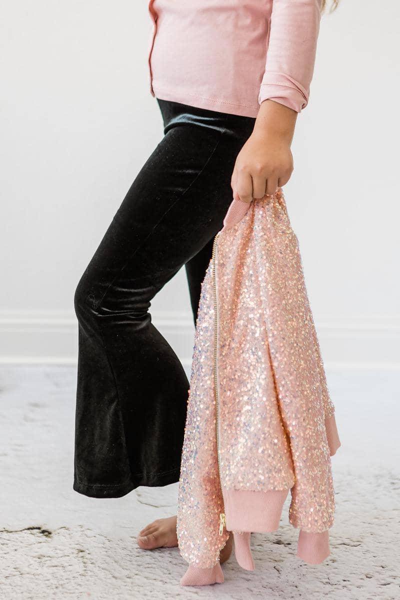 girls black velvet bells pants paired with pink shirt holding a pink sequin jacket
