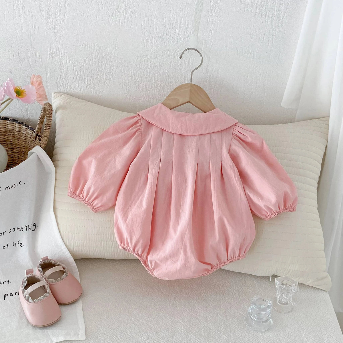 Pink baby girl bubble romper with puff sleeves and peter pan collar hanging on wooden hanger