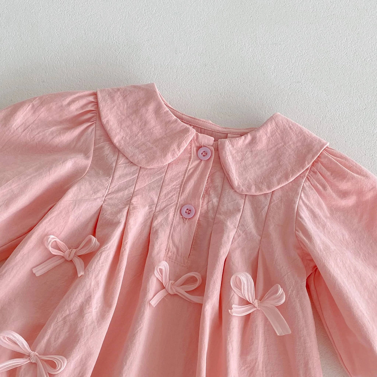 Pink baby girl bubble romper with peter pan collar, buttons, and decorative bows on soft fabric