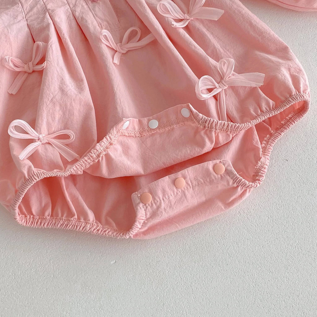 Close-up of pink baby girl bubble romper with bows and snap buttons for easy diaper changes