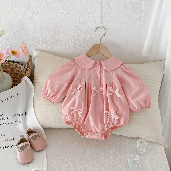 Pink baby girl bubble romper with puff sleeves and bow details hanging on wooden hanger