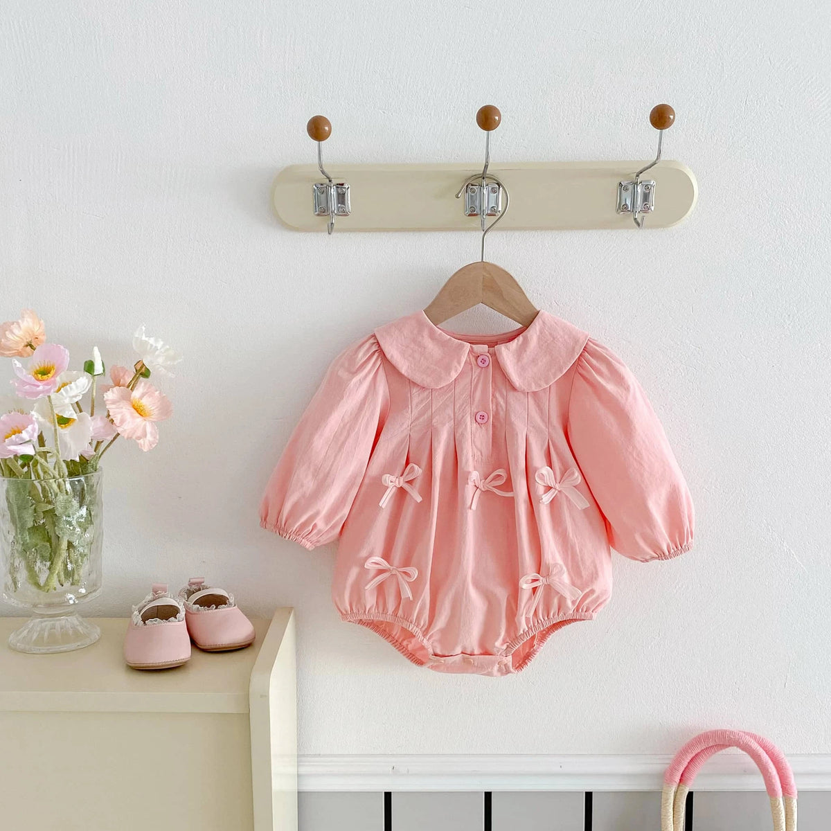 Pink baby girl bubble romper with long sleeves and bow details hanging on wooden hanger