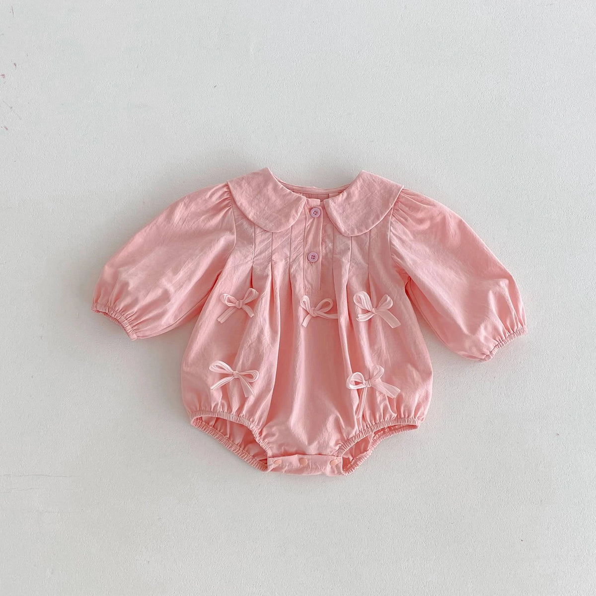 Pink baby girl bubble romper with long sleeves and decorative bows for infants