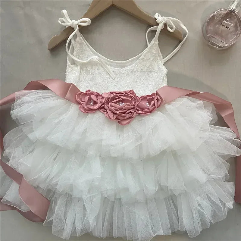 White vintage girl dress with lace top, tiered tulle skirt, and pink floral sash for infants