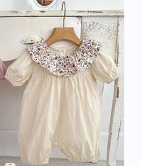 Cream vintage floral baby romper with puff sleeves and floral ruffle collar hanging on wooden hanger