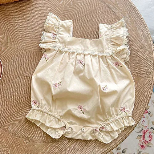 cream vintage floral baby romper with pink flowers for infants laid flat on wooden table