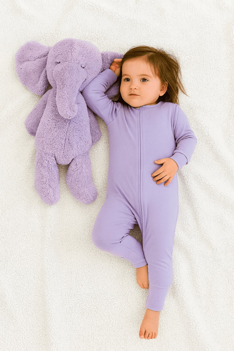 Child in a purple onesie holding a purple stuffed elephant on a white background