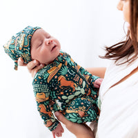 The SoftKnot Cap in Wild West print on a sleeping newborn cradled by mom, cozy bamboo fabric.