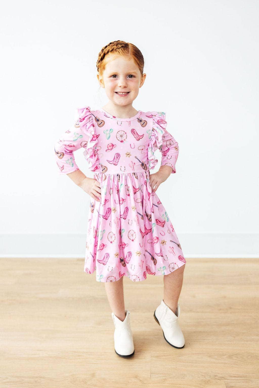 Girl wearing pink kids twirl ruffle dress with cowboy boots standing hands on hips western dress for girls