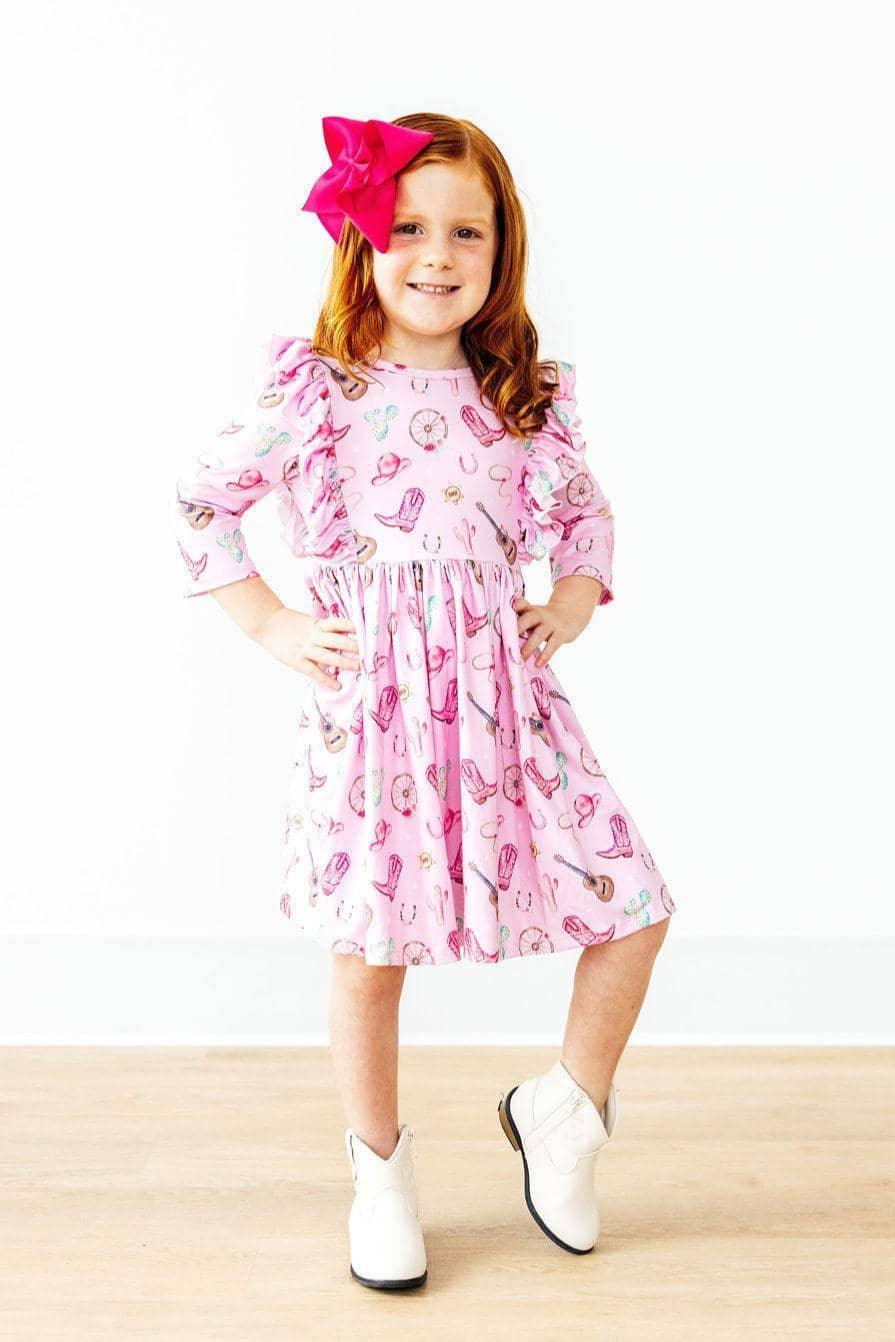 young girl wearing pink kids twirl ruffle dress with cowboy boots and large pink hair bow posing confidently western dress for girls
