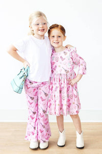 Two young girls standing, one wearing pink western dress for girls with ruffle sleeves, and the other in matching pink pants