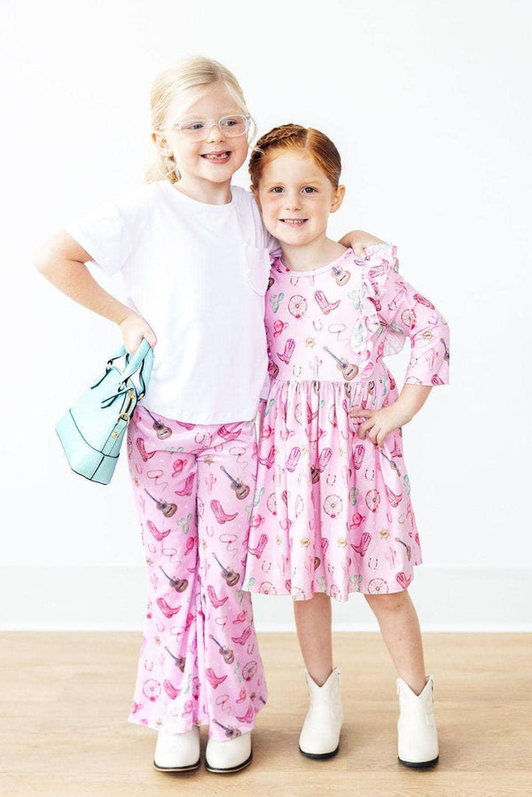 Two young girls standing, one wearing pink western dress for girls with ruffle sleeves, and the other in matching pink pants