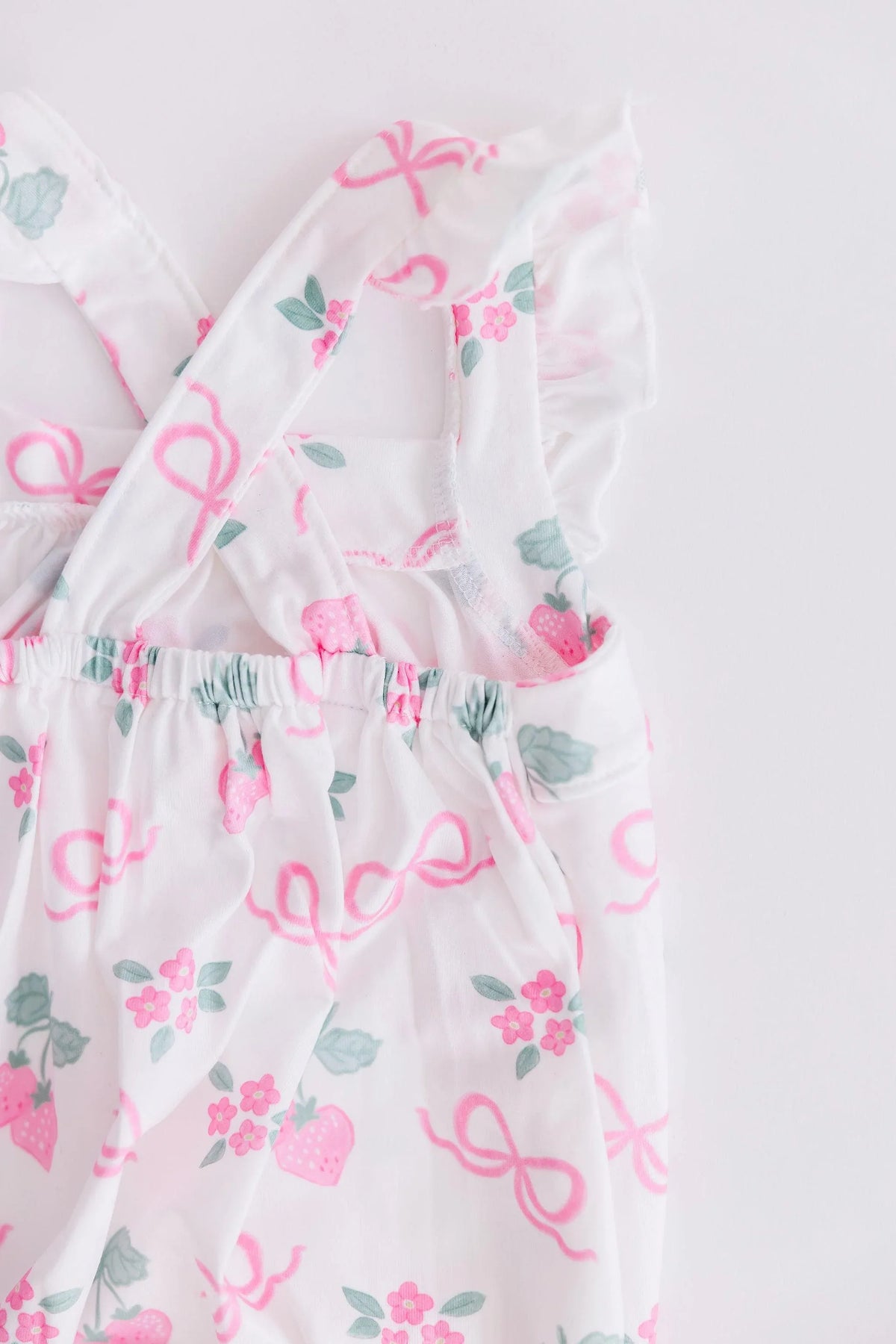 White ruffle cross back romper for little girls with pink strawberries and bows pattern, toddler size