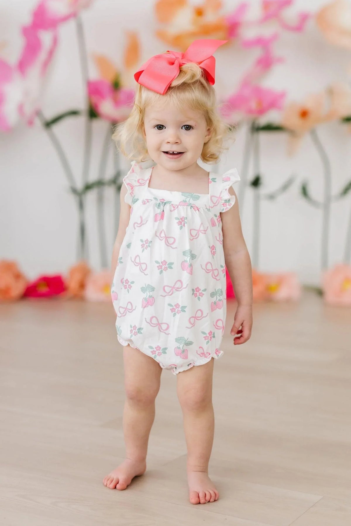 Little girl wearing white ruffle cross back romper for little girls with pink bow and floral print