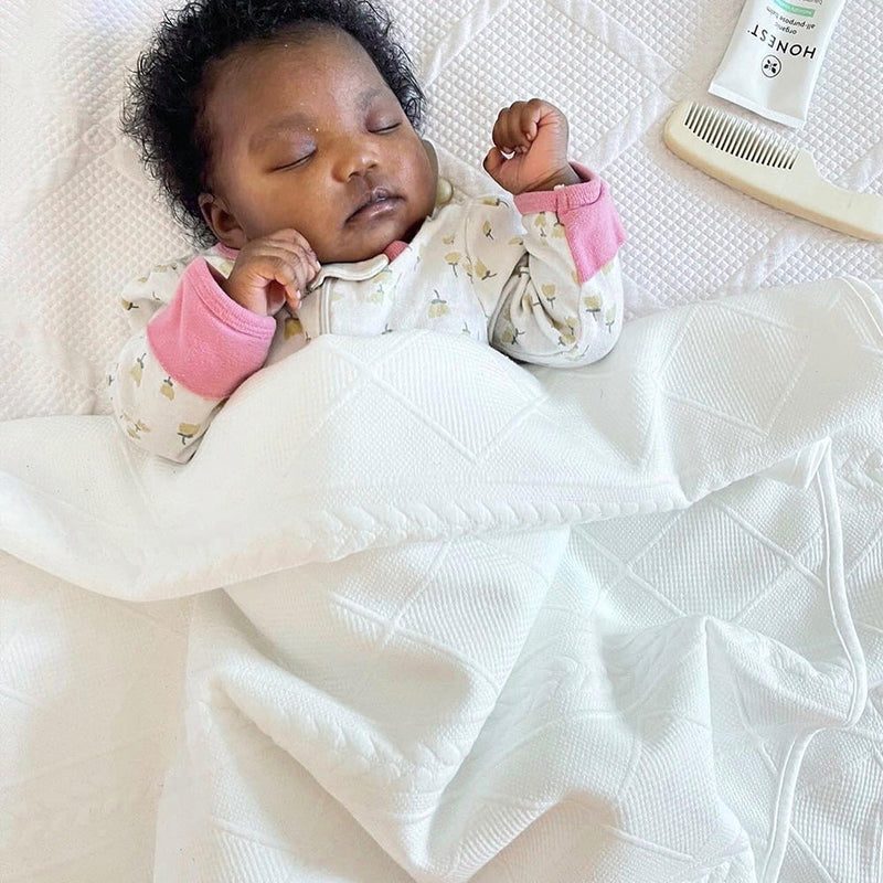 A peaceful baby sleeping wrapped in the White 50" x 60" Full Size Knit Throw by Goosewaddle®, highlighting its comfort and warmth, perfect for newborns.